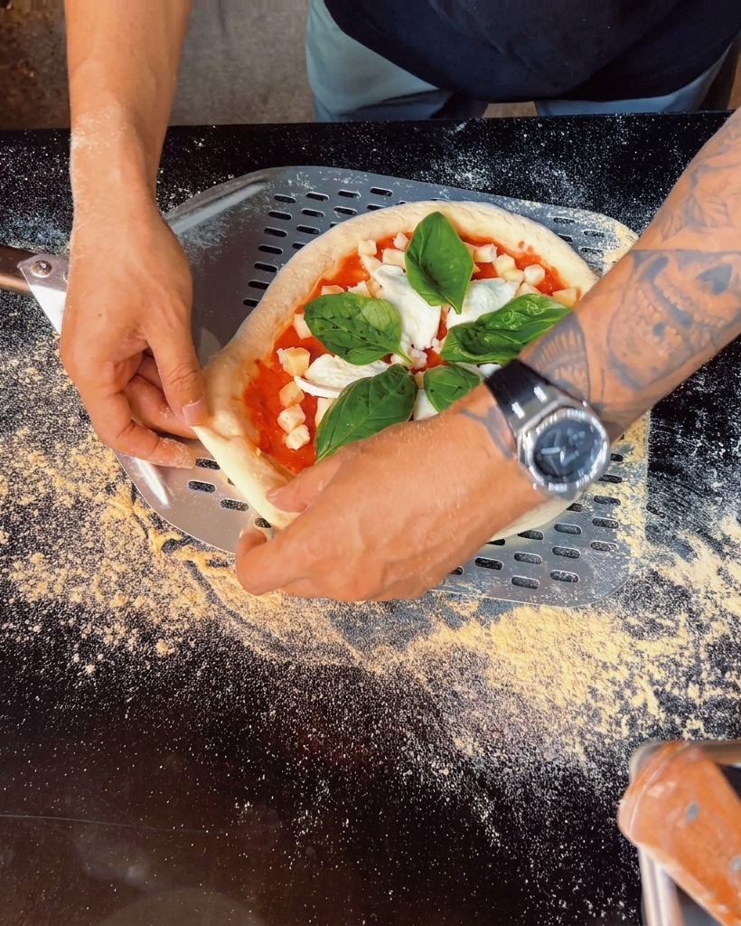 Dettaglio di fresche foglie di basilico aggiunte sulla pizza appena farcita.