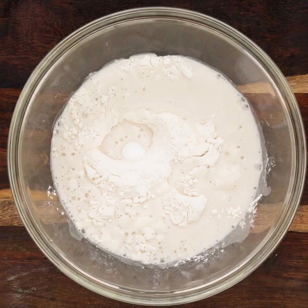 Gli ingredienti liquidi e secchi combinati in una ciotola di vetro, che formano un impasto grezzo.
