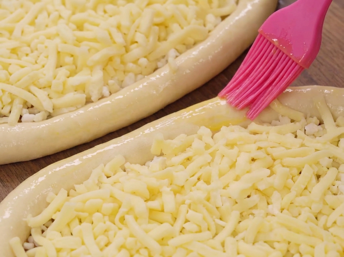 Un pennello in silicone rosa che applica olio sul bordo di una barchetta di pasta ripiena di mozzarella.