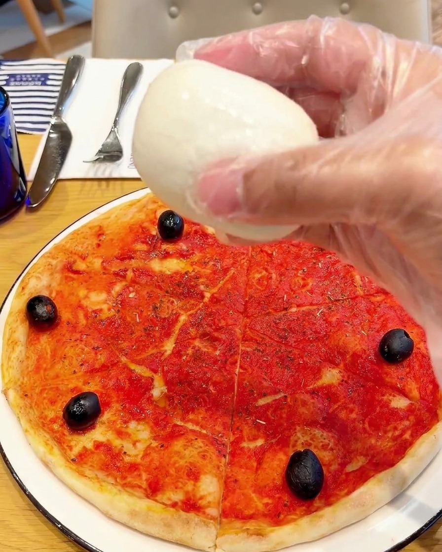 Pezzetti di mozzarella di bufala fresca distribuiti sulla pizza.