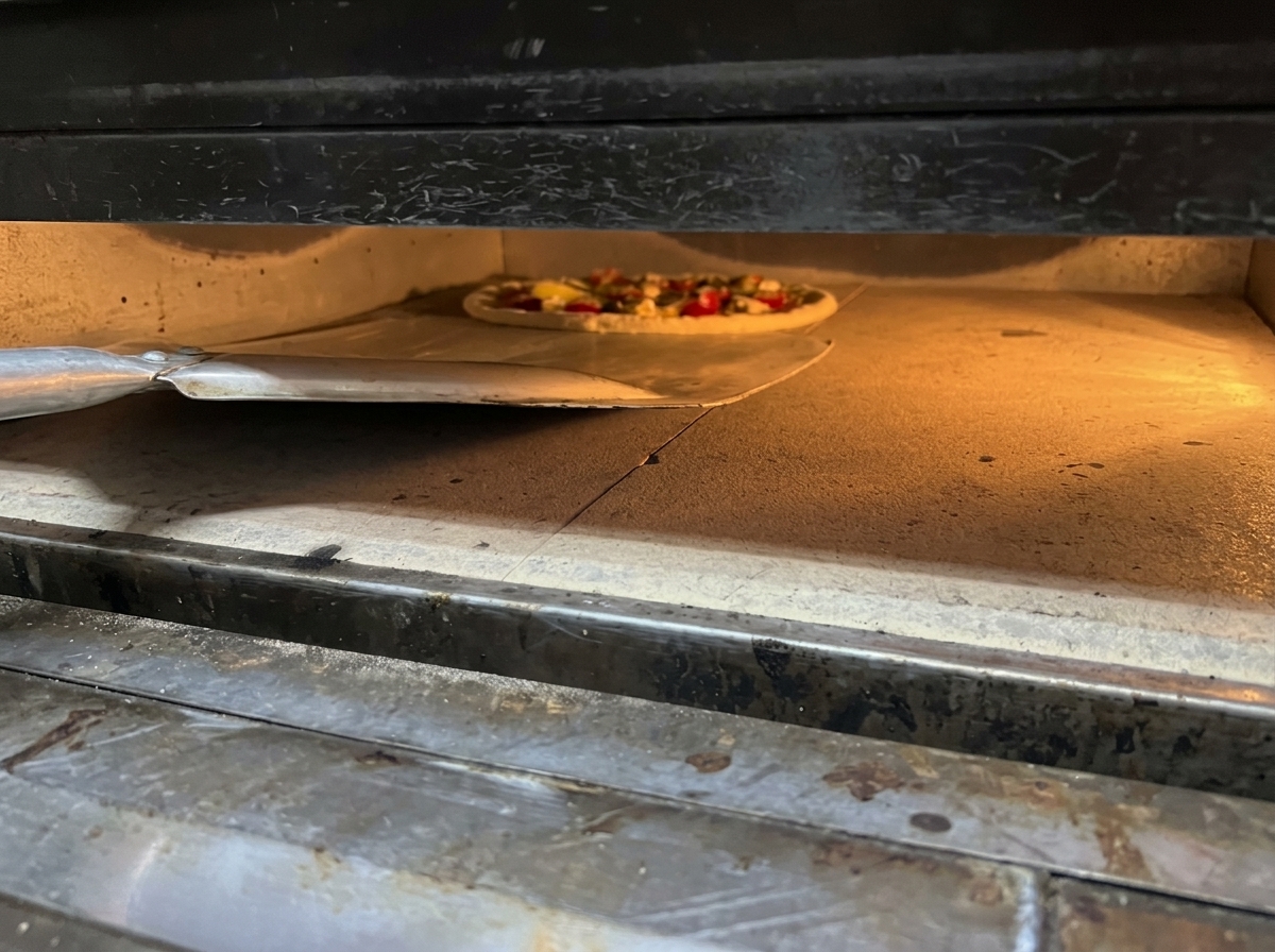 Pizza assemblata che scivola da una pala nel forno caldo.