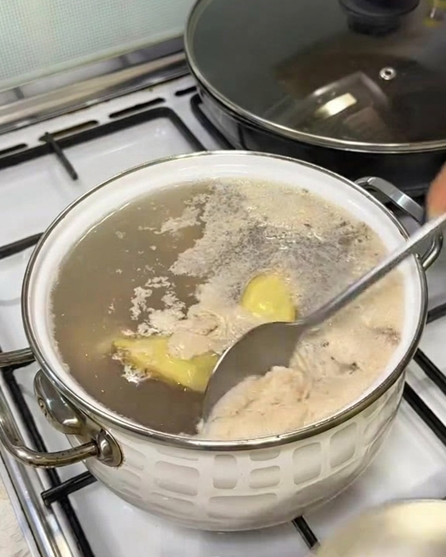 Un cucchiaio che rimuove la schiuma grigiastra dalla superficie dellacqua bollente.