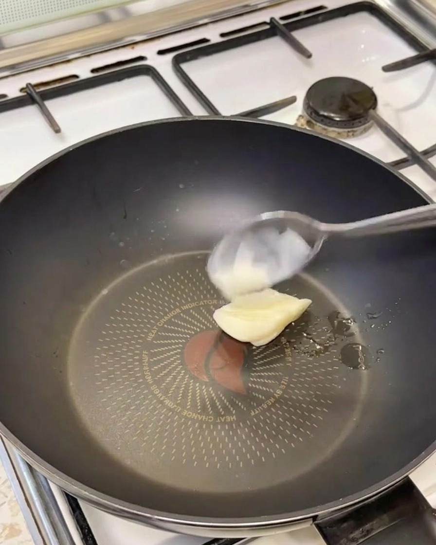 Un cucchiaio di strutto bianco che si scioglie in una padella nera calda.