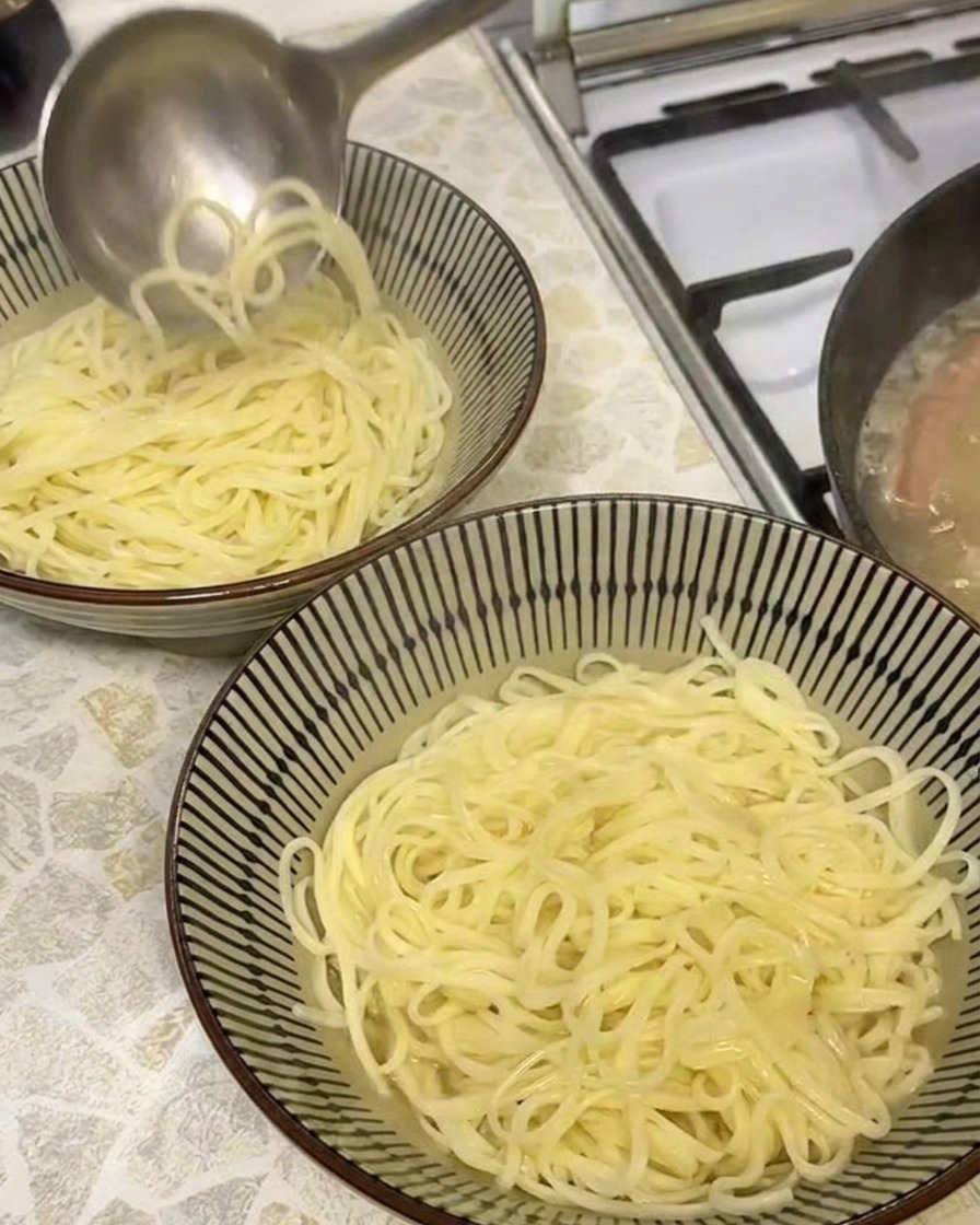 Un mestolo che versa brodo di maiale dorato e opaco in una ciotola con noodles ramen appena cotti.