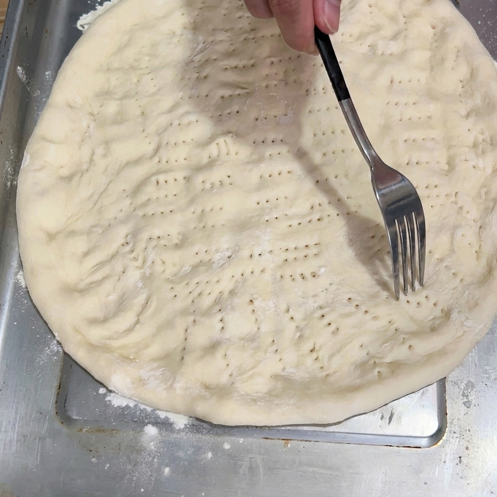 Una forchetta che punge la base dellimpasto appiattito sulla teglia.