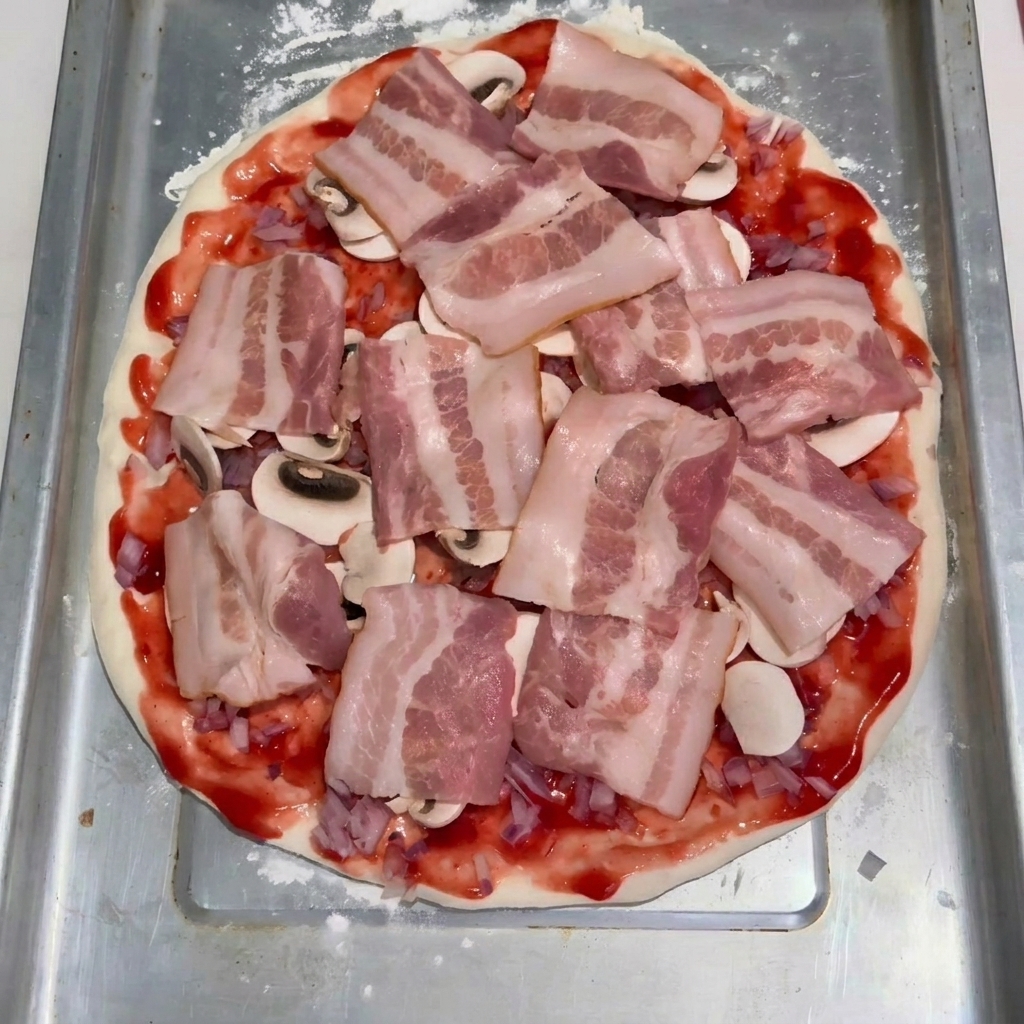 Fette di pancetta cruda disposte ordinatamente sopra i funghi e la salsa di pomodoro sulla base dellimpasto.