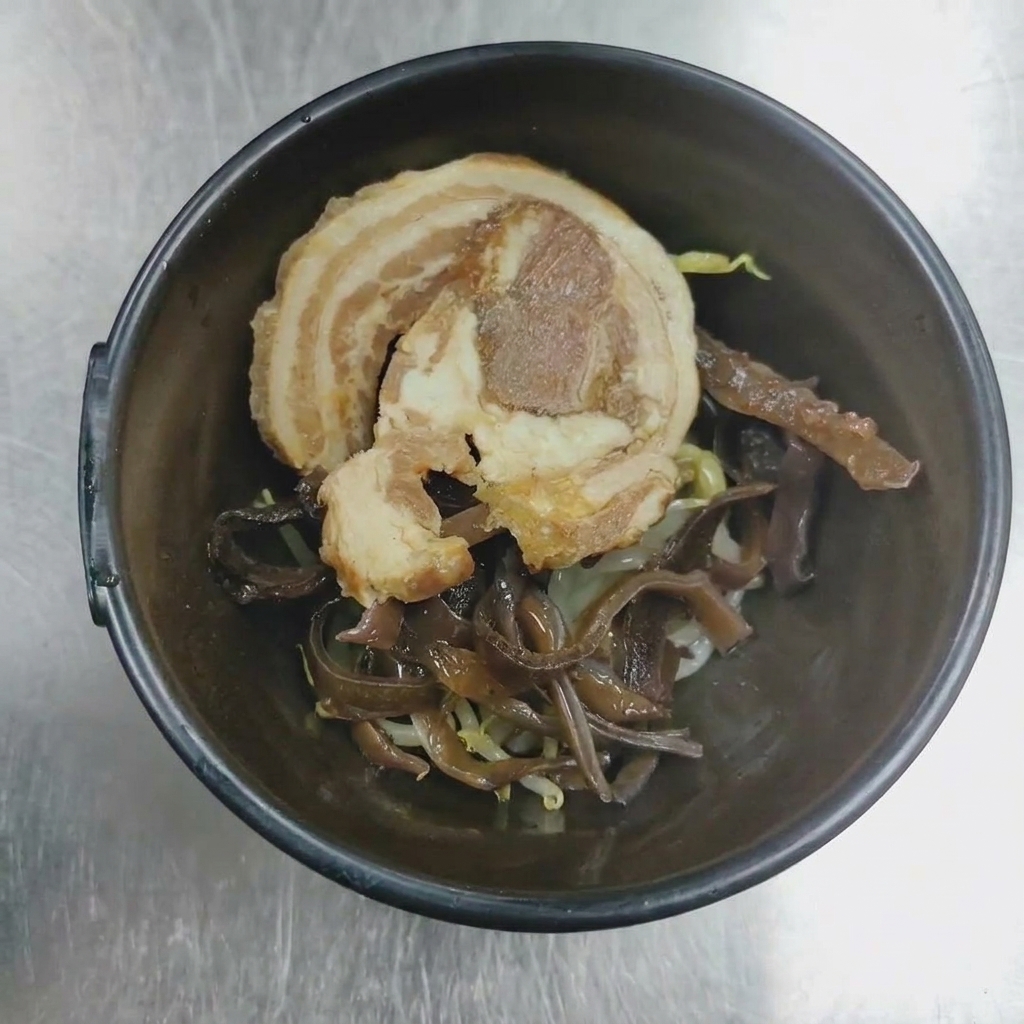 Primo piano di una ciotola con chashu di maiale e funghi wood ear pronti per essere serviti.