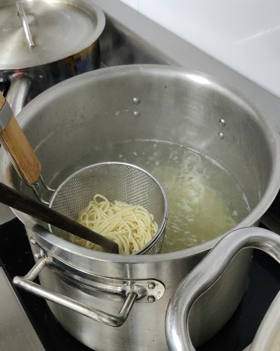 Noodles da ramen che bollono in un cestello dacciaio immerso in una pentola dacqua.