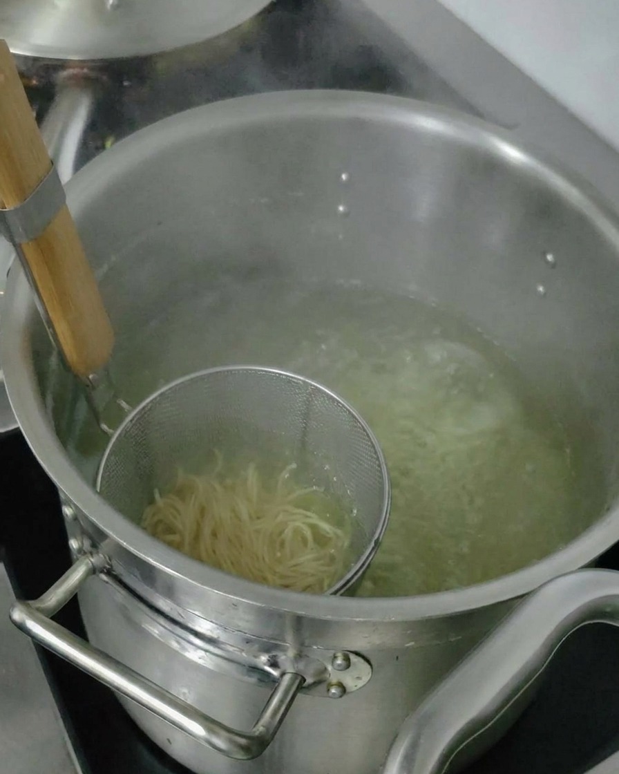 Noodles cotti sollevati nel colino per drenare lacqua in eccesso prima di unirli alla zuppa.