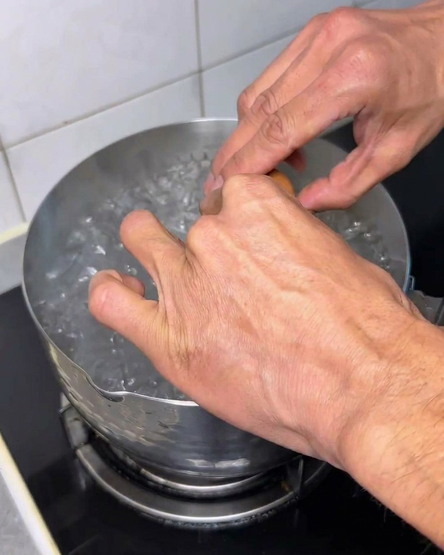Un uovo crudo aperto in una pentola di acqua bollente.