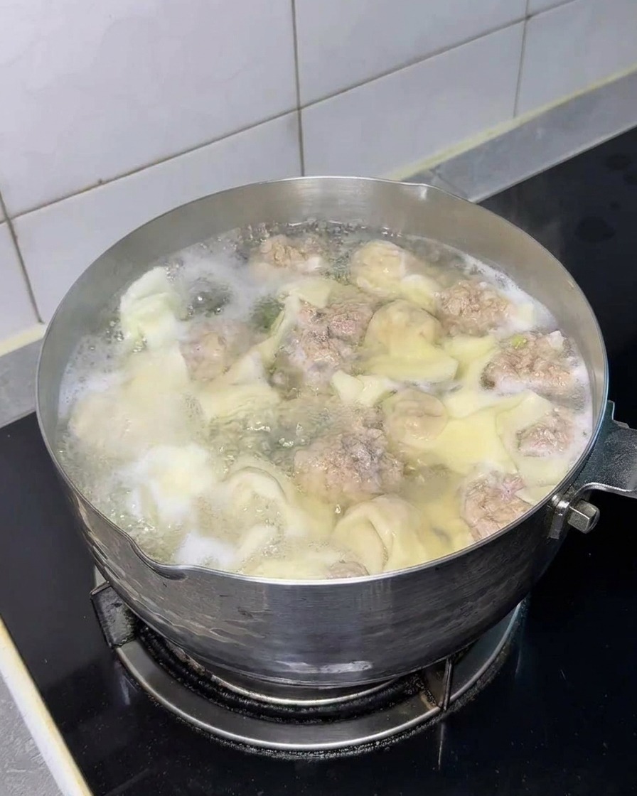 Un blocco quadrato di noodle istantanei secchi immerso nella pentola con wonton e polpette.