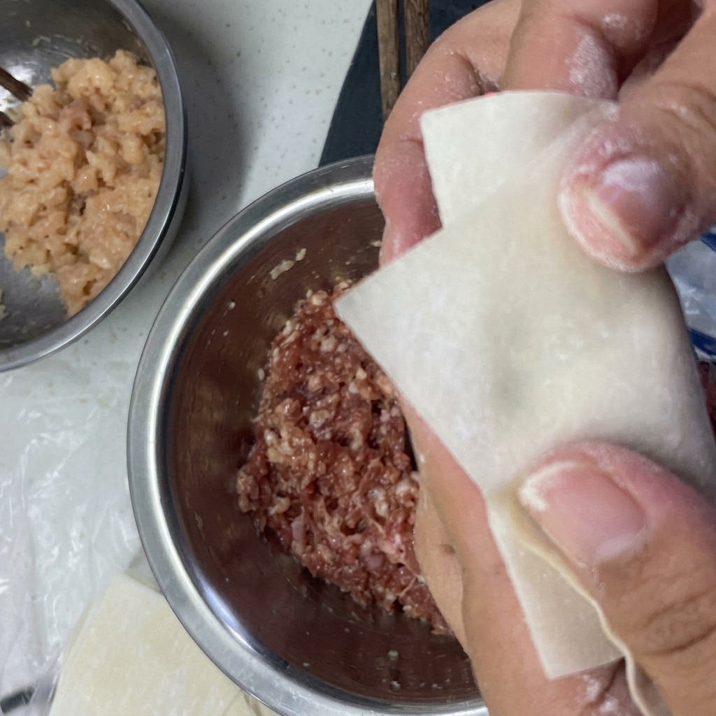 Mani che piegano un foglio per wonton attorno al ripieno e ne sigillano i bordi con acqua.