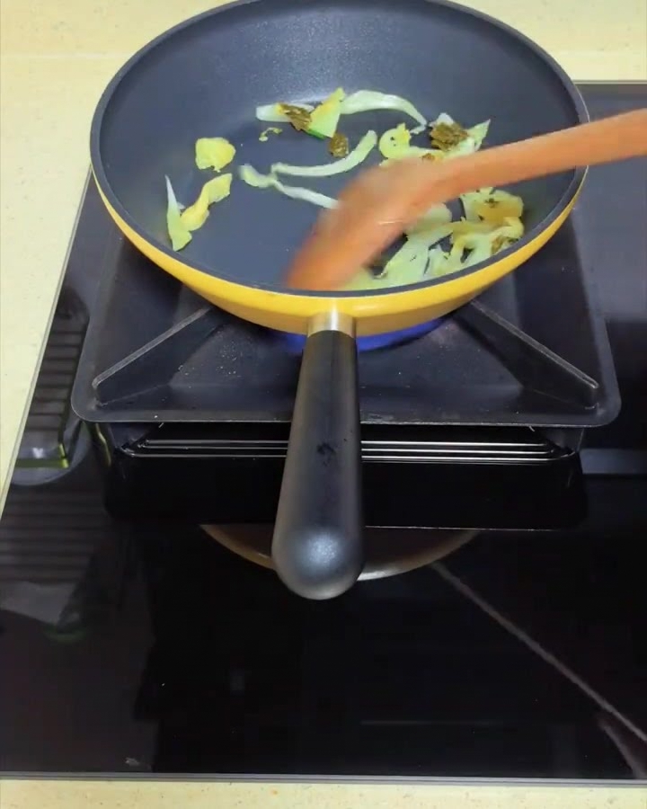 Foglie di senape in salamoia saltate in una padella gialla con una spatola di legno.