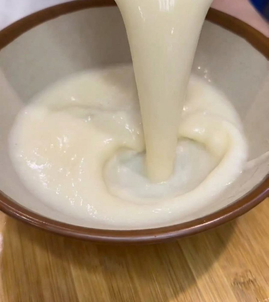 Zuppa di ramen cremosa e bianca versata da una caraffa in una ciotola di ceramica dal bordo marrone.
