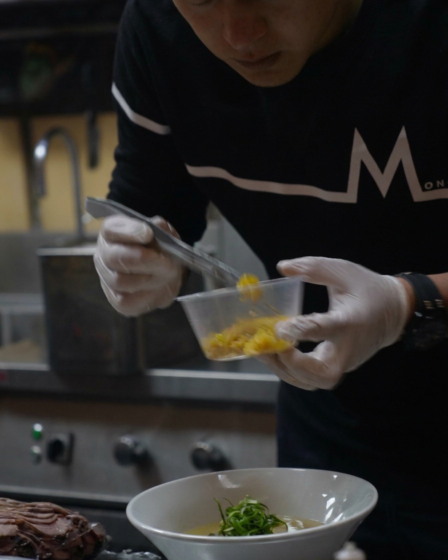 Un cucchiaino di scorza di yuzu giallo brillante cosparso sul ramen finito.