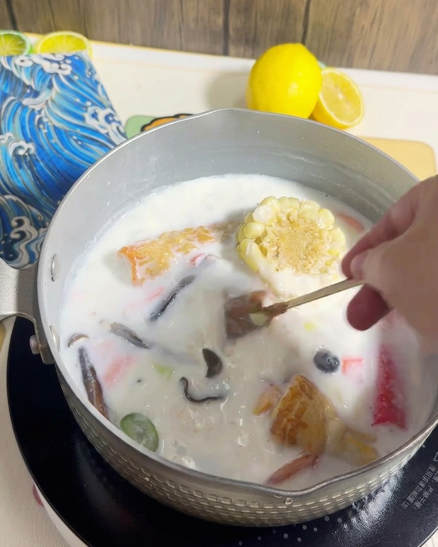 Noodle ramen aggiunti a una pentola piena di brodo cremoso e vari condimenti cotti.