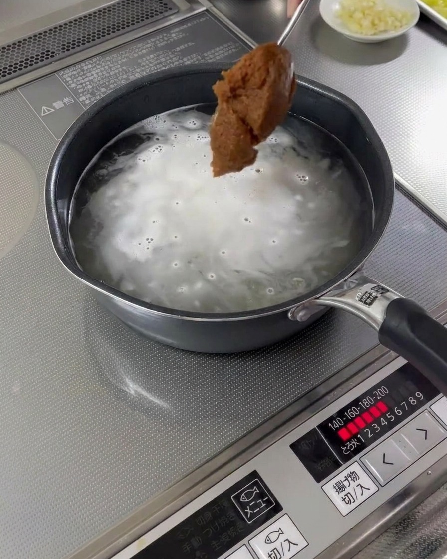 Un cucchiaio di pasta di miso aggiunto a una pentola di brodo bollente.