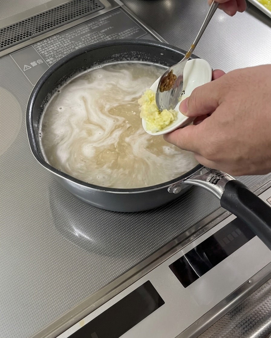 Aglio e zenzero grattugiati aggiunti a una base di zuppa in ebollizione.