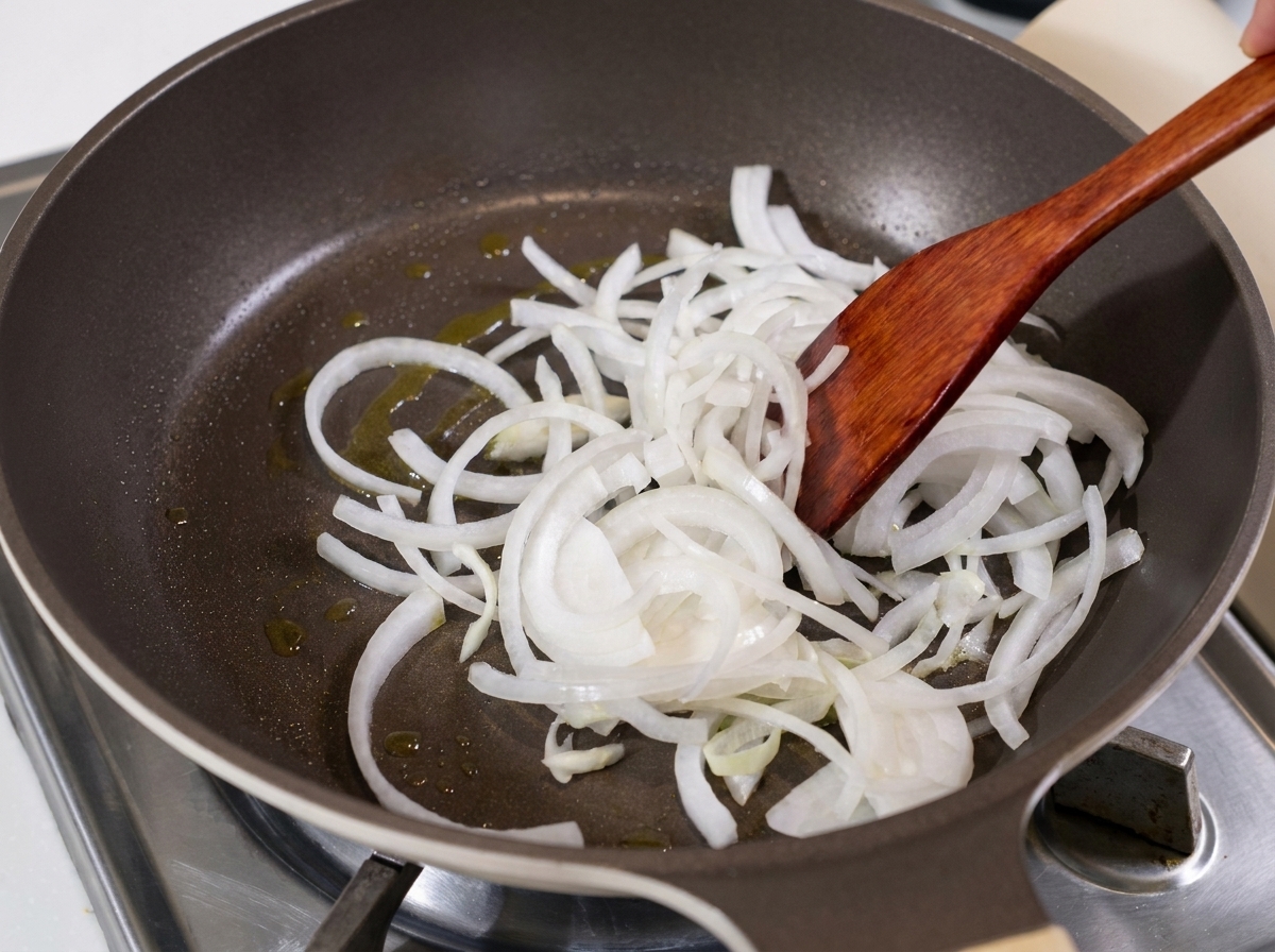 Cipolle bianche affettate saltate in padella con olio usando una spatola di legno.