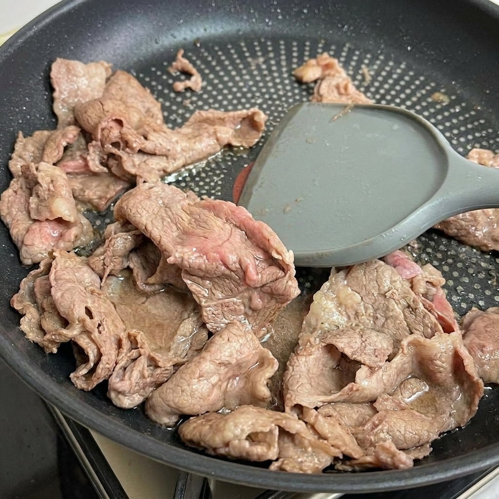 Il manzo rosolato viene sollevato dalla padella con una spatola.