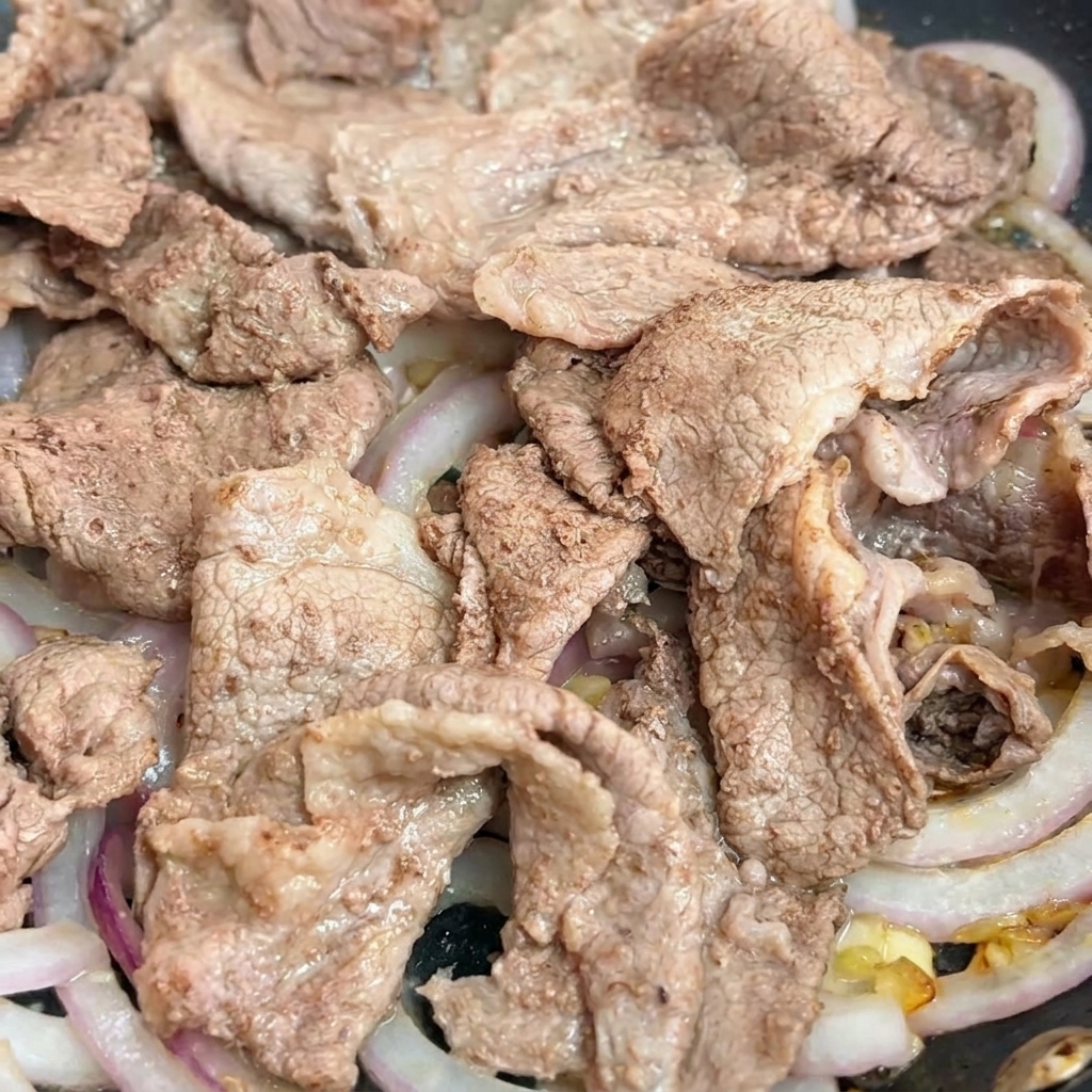 Salsa teriyaki versata in padella sopra il manzo e le cipolle.