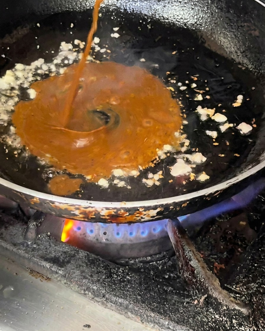 Salsa scura versata nella padella con il soffritto di aglio e cipolla.