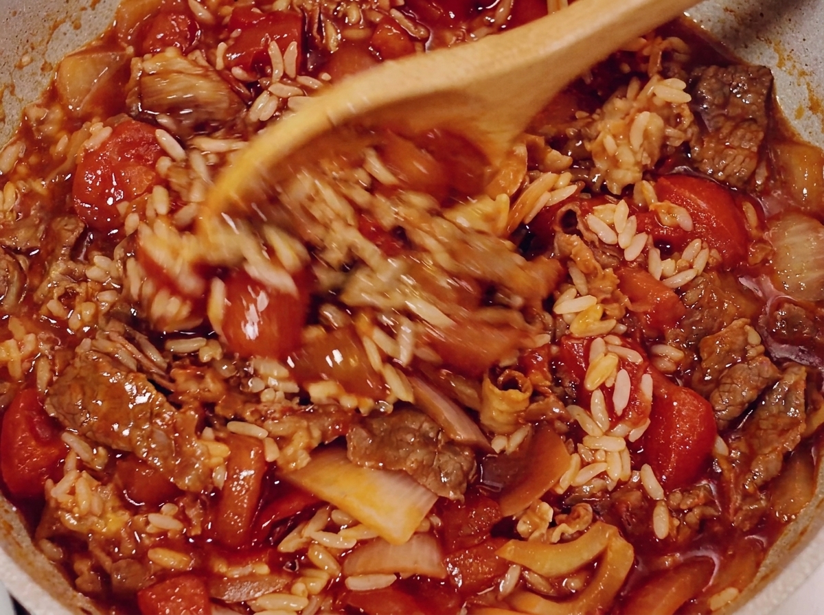 Un cucchiaio di legno che mescola manzo, riso e salsa di pomodoro in padella.
