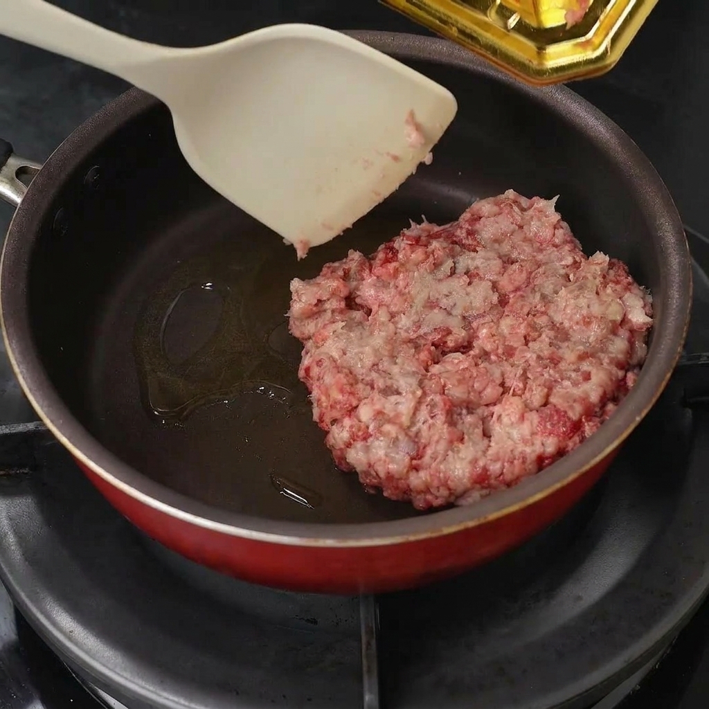 Manzo macinato inserito nella padella con olio e sgranato con una spatola.