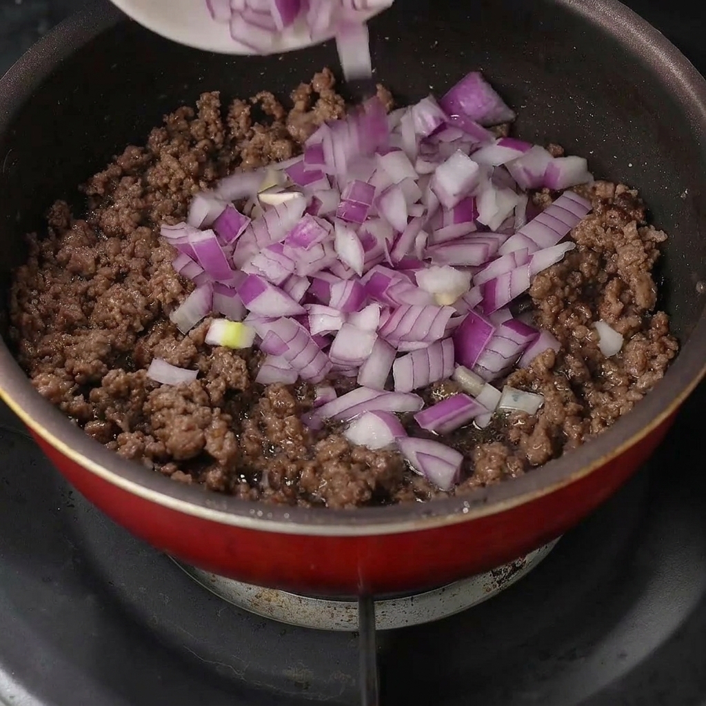 Cipolle viola tritate aggiunte al manzo cotto nella padella.