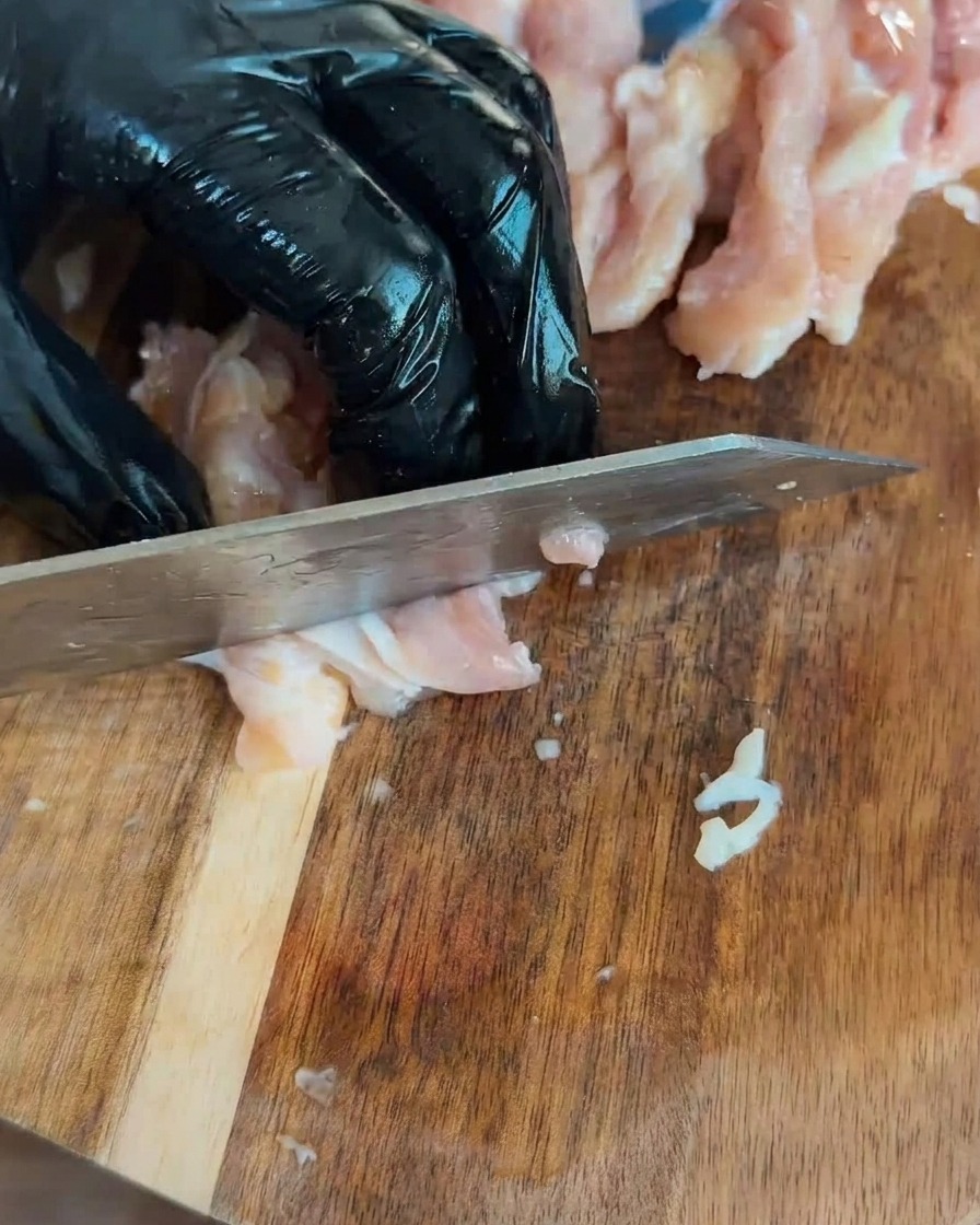 Pezzi di pollo crudo tagliati a cubetti disposti su un tagliere di legno.