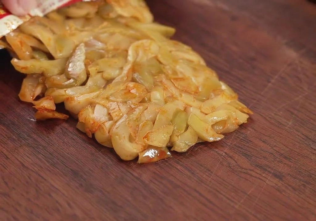Una bustina di verdure senapate conservate versate su un tagliere di legno, pronte per essere tritate.