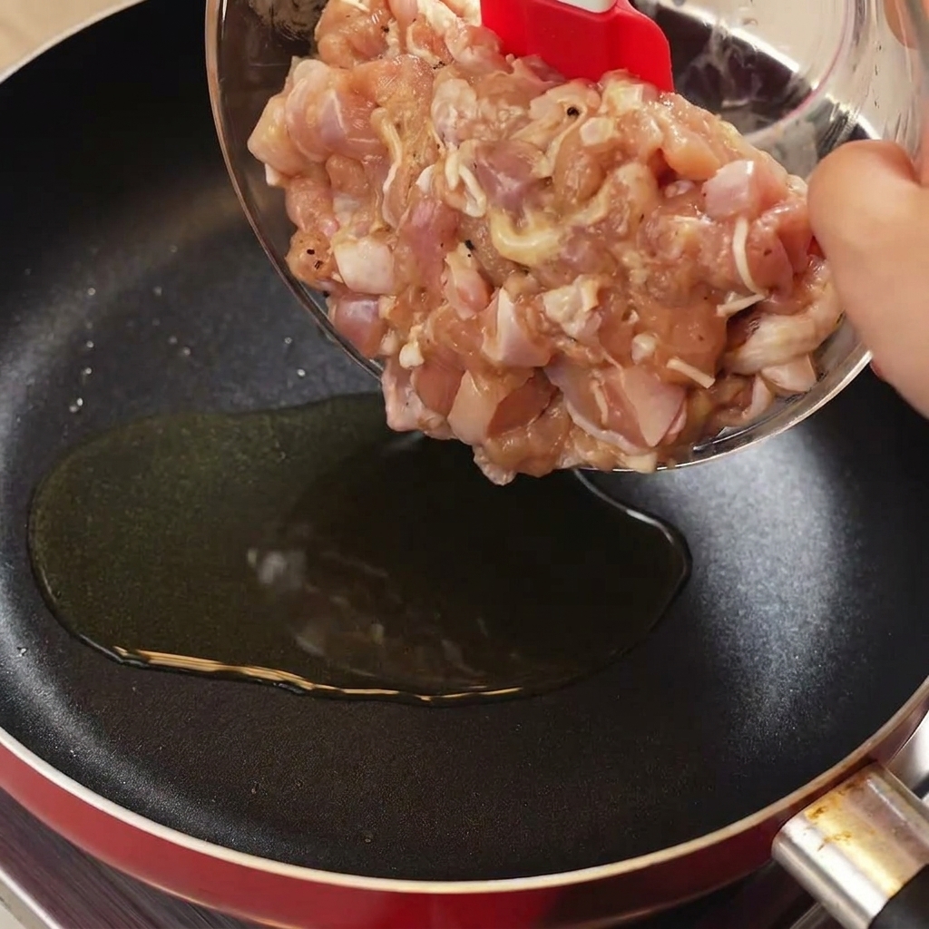 Uso di una spatola rossa per trasferire i pezzi di pollo crudo marinato dalla ciotola in una padella calda con olio.