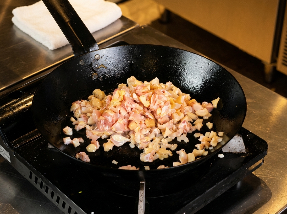 Pollo a dadini e cartilagine in cottura allinterno di una padella scura.
