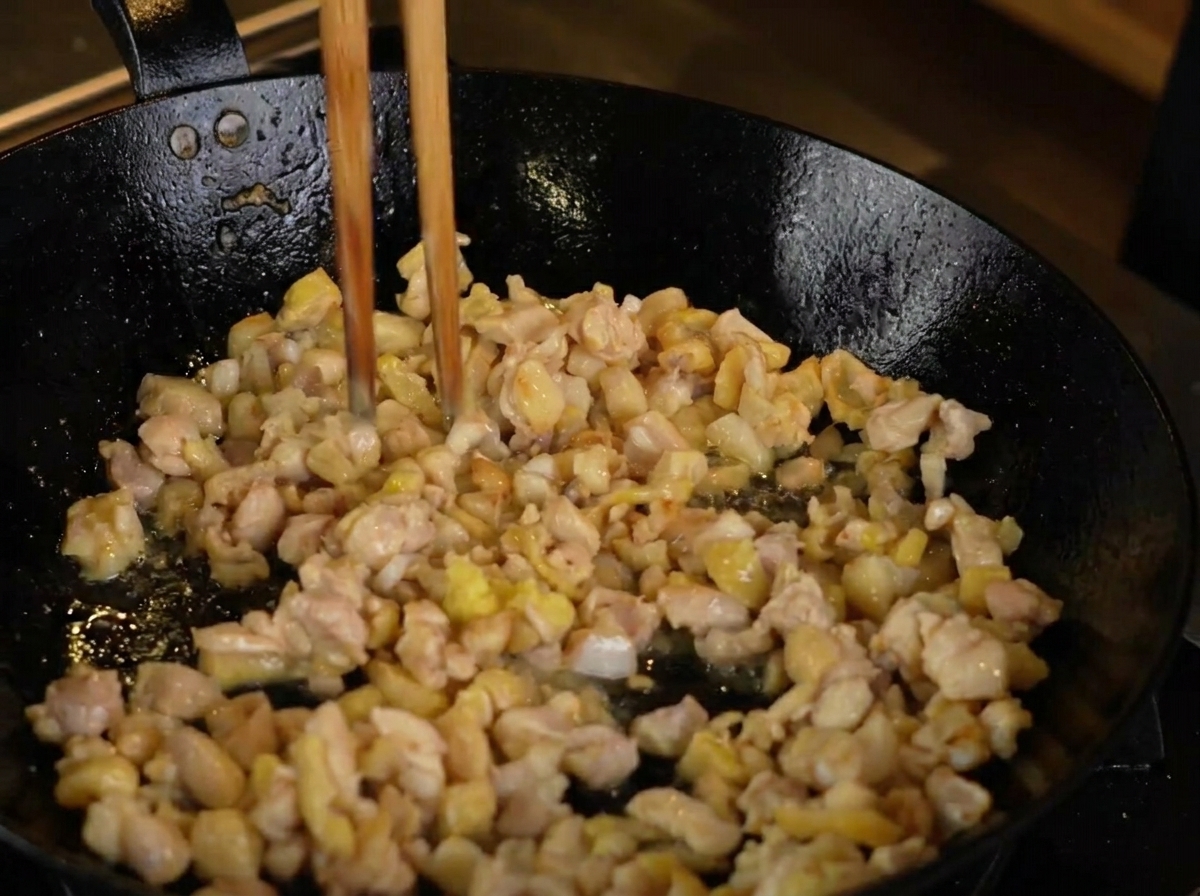 Zenzero grattugiato che si unisce ai pezzi di pollo in doratura in una padella calda.
