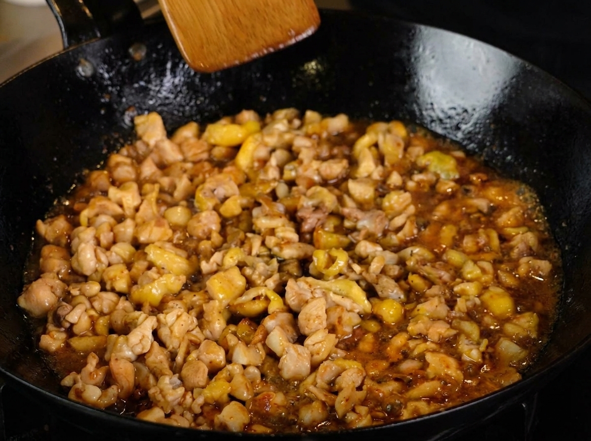 Pollo a dadini che cuoce a fuoco lento in una ricca salsa scura, spolverato con pepe nero e mescolato con una spatola di legno.