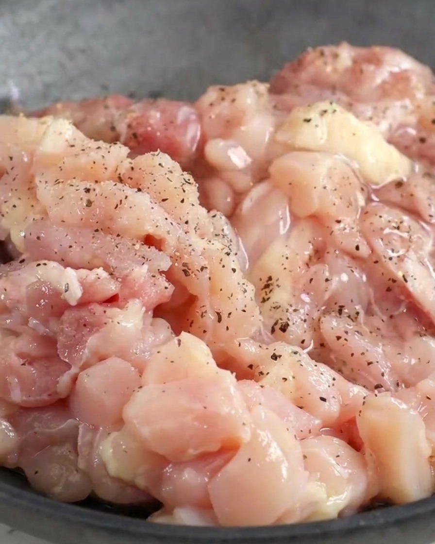 Pollo tritato crudo in una ciotola cosparso di pepe nero e condimenti liquidi.