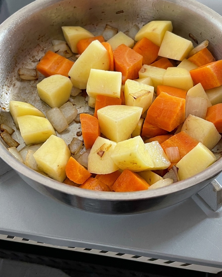 Acqua limpida versata in una padella contenente cipolle, carote e patate soffritte.