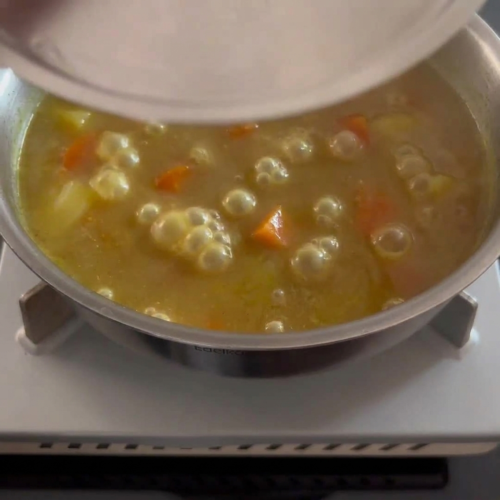 Una salsa al curry densa e dorata mescolata con pezzi di patate e carote visibili.
