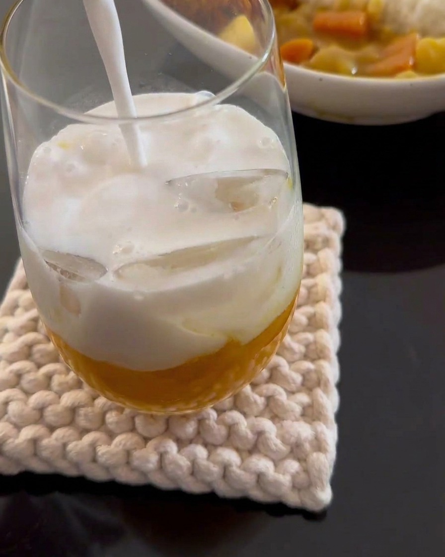 Latte di cocco bianco versato in un bicchiere alto contenente purea di mango gialla e cubetti di ghiaccio.