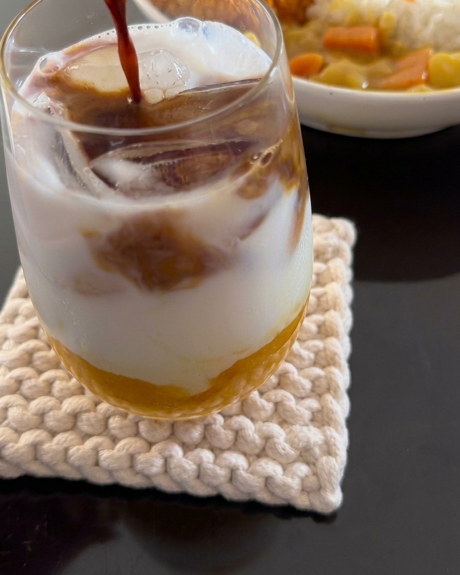 Primo piano di espresso versato in una bevanda a strati composta da polpa di mango, latte di cocco e ghiaccio.