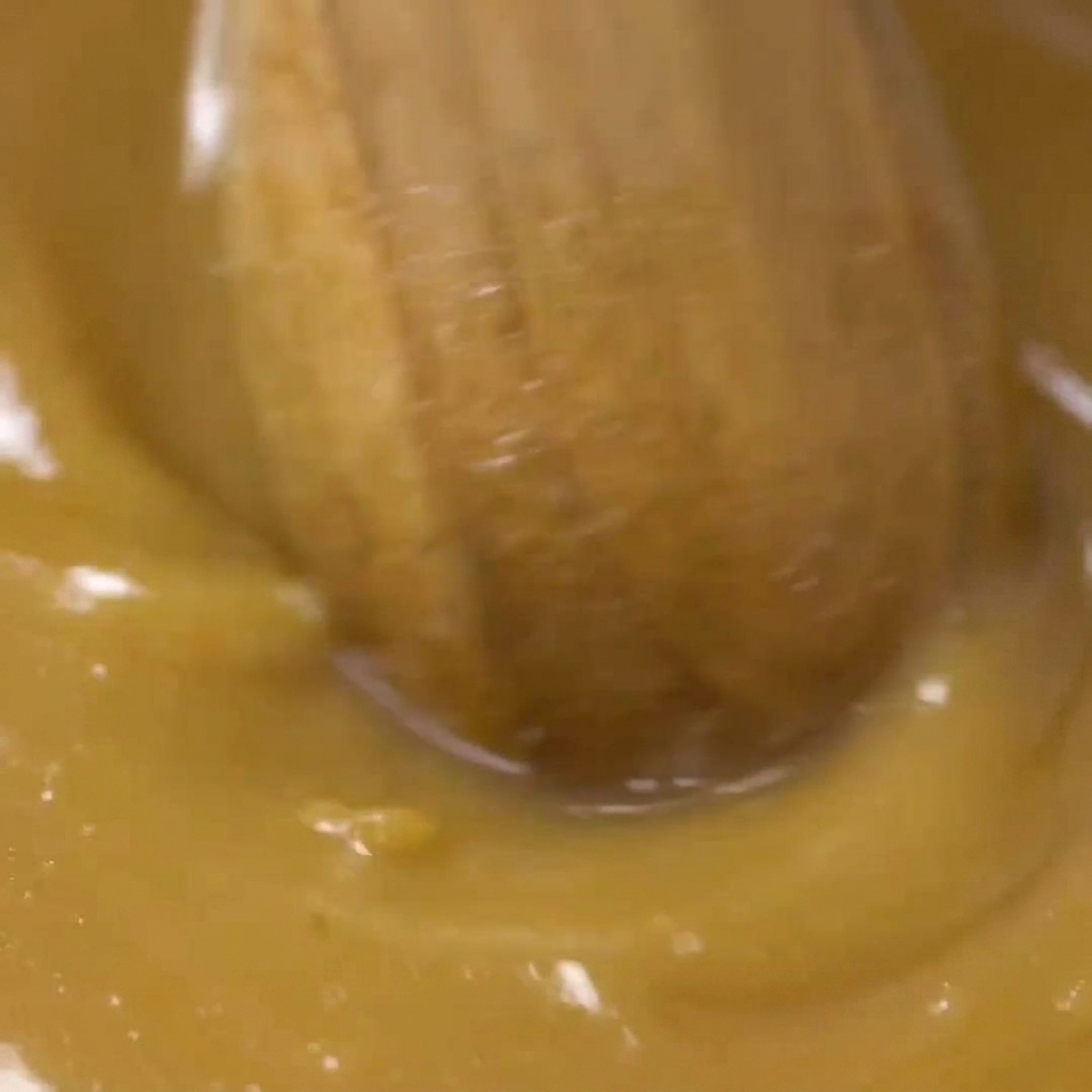 Un cucchiaio di legno che mescola la marinata di miso dorata in una ciotola fino a renderla uniforme.
