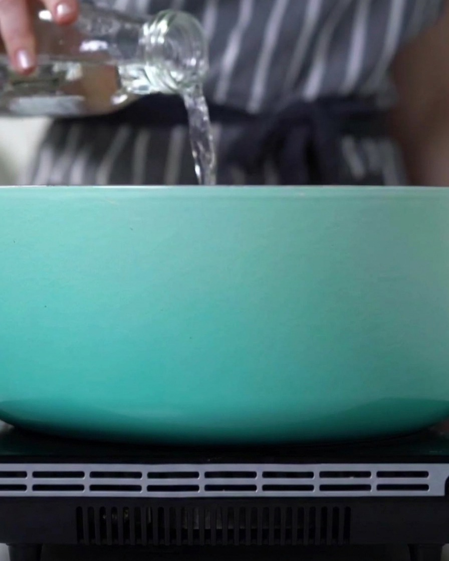 Acqua versata da una bottiglia di vetro in una pentola blu chiaro sul fornello.