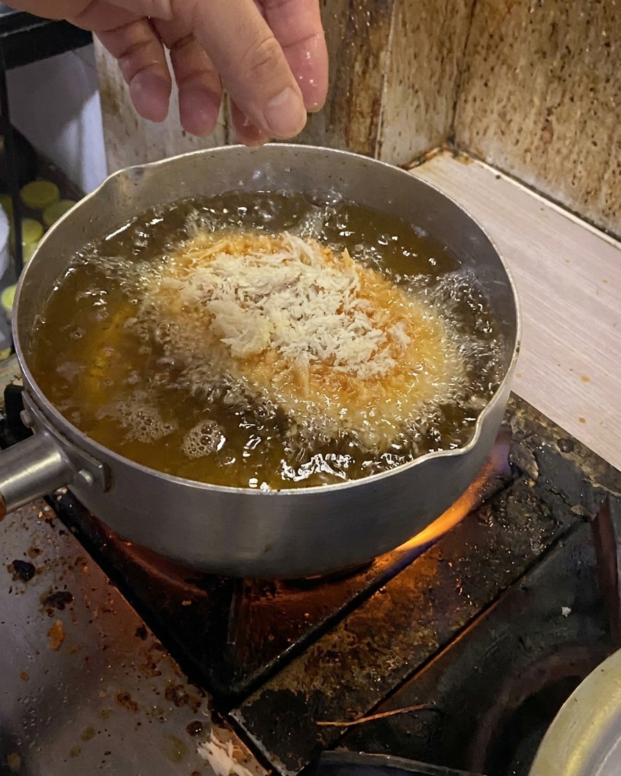 Una cotoletta di maiale impanata che viene delicatamente immersa in una pentola di olio bollente.