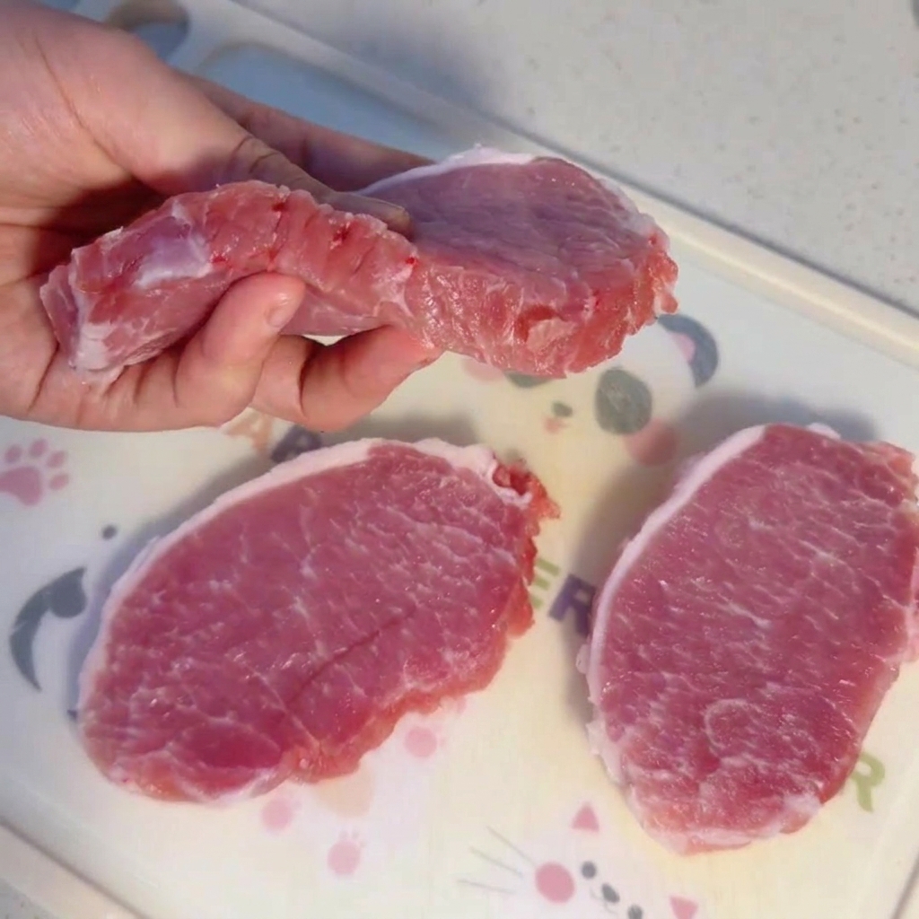 Spesse fette di lonza di maiale cruda su un tagliere.