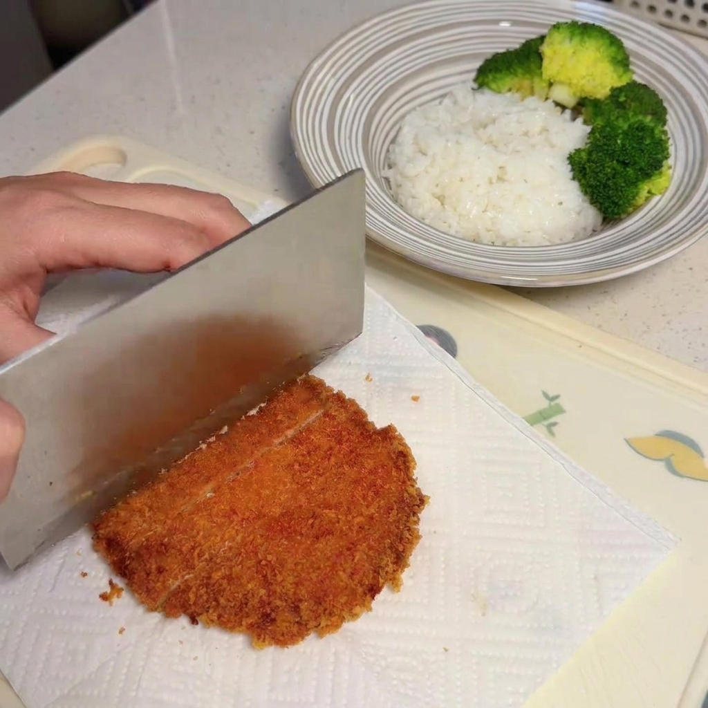 Un coltello che taglia una cotoletta dorata su carta assorbente.