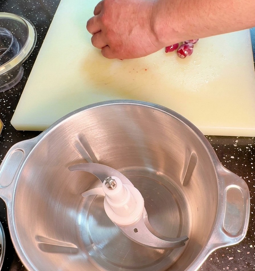 Un primo piano di una mano che trita finemente una cipolla rossa su un tagliere bianco con un grande coltello da cucina.