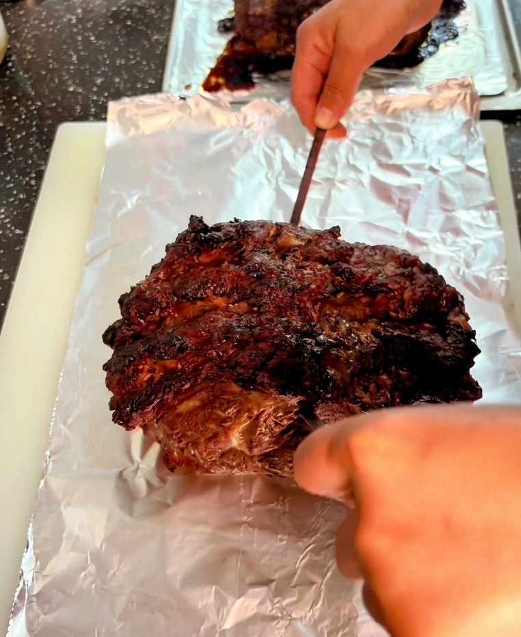 Uno spiedino di metallo che fora la superficie scura di un grande arrosto di manzo appoggiato su carta stagnola.