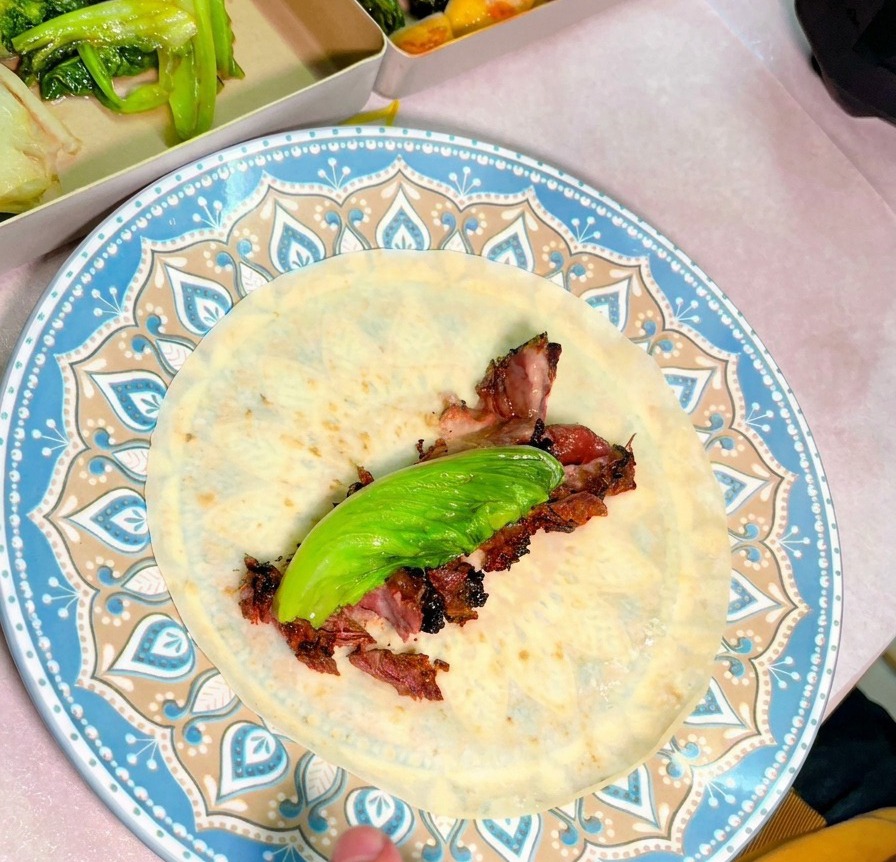 Vista dallalto di un piatto con una tortilla farcita con fette succose di manzo affumicato e una foglia verde fresca.