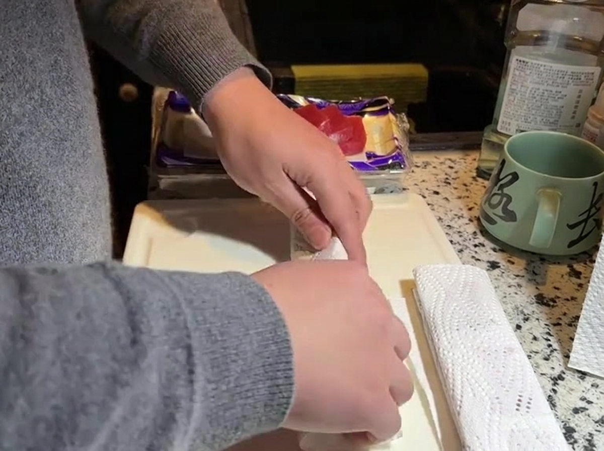 Mani che premono carta da cucina bianca contro un blocco di tonno rosso crudo su un tagliere bianco.