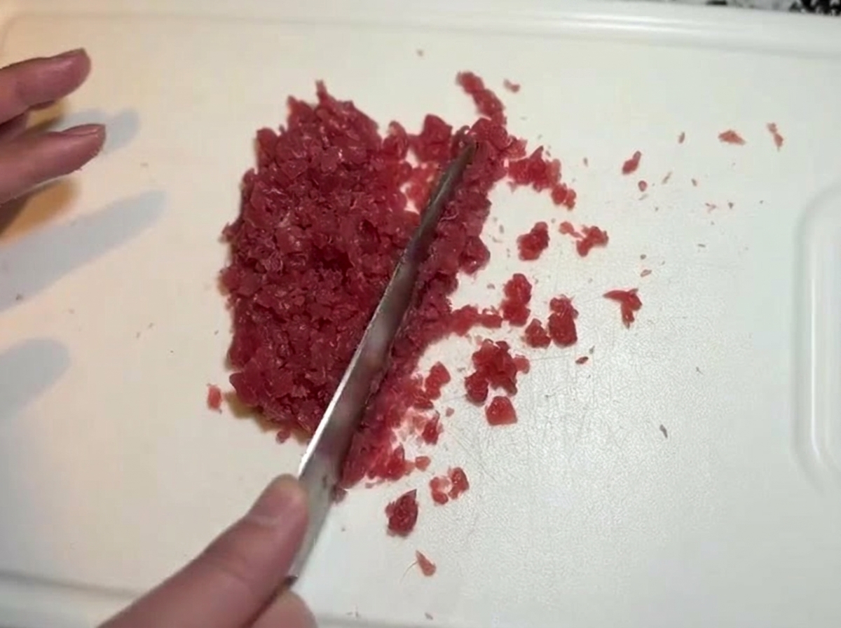 Un coltello che trita finemente pezzi di tonno rosso crudo su un tagliere.